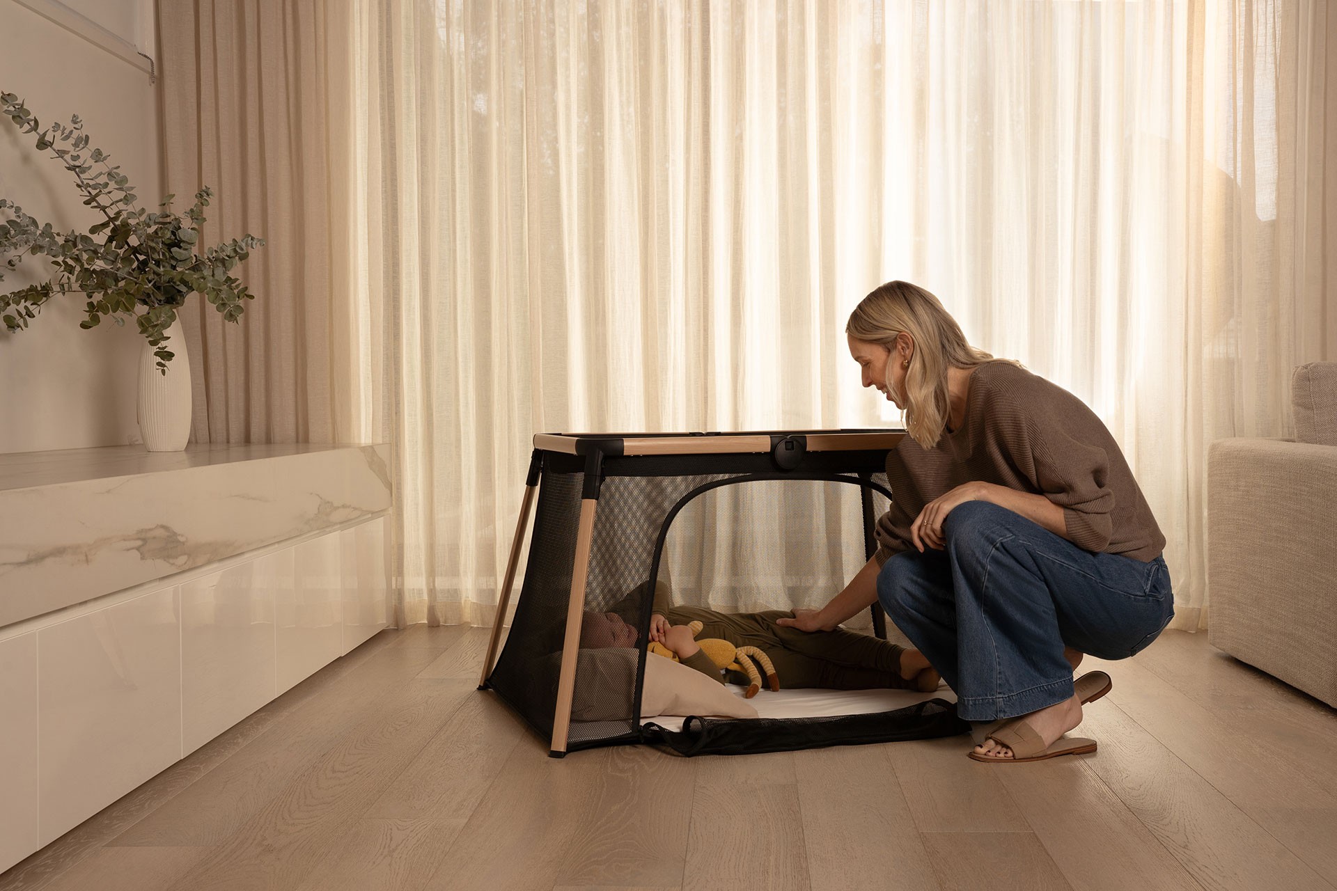 Mum comforting her toddler inside a secure travel cot with an open side zip panel designed for safe access, a feature valued in the best travel cot Australia.