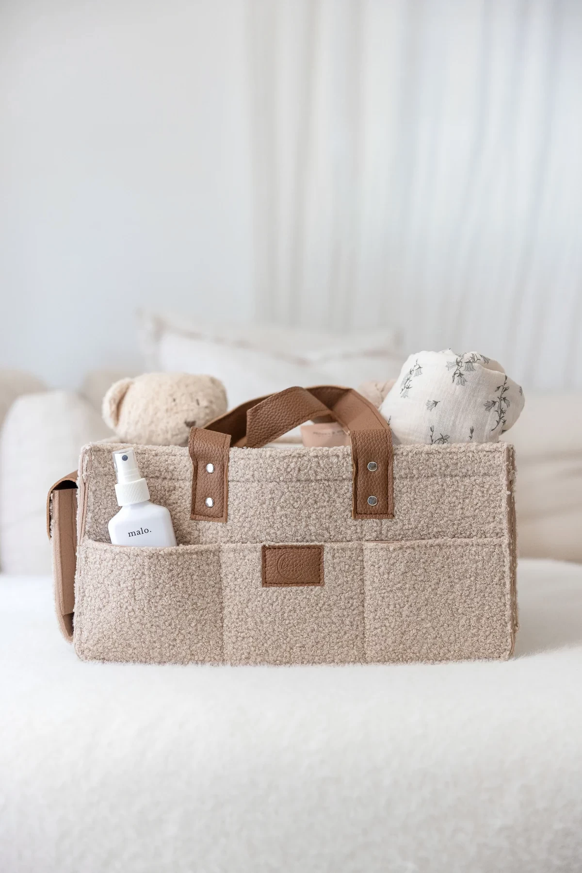 The Linen Label nappy caddy shown in beige, with baby items in it, in front of a sheer white curtain