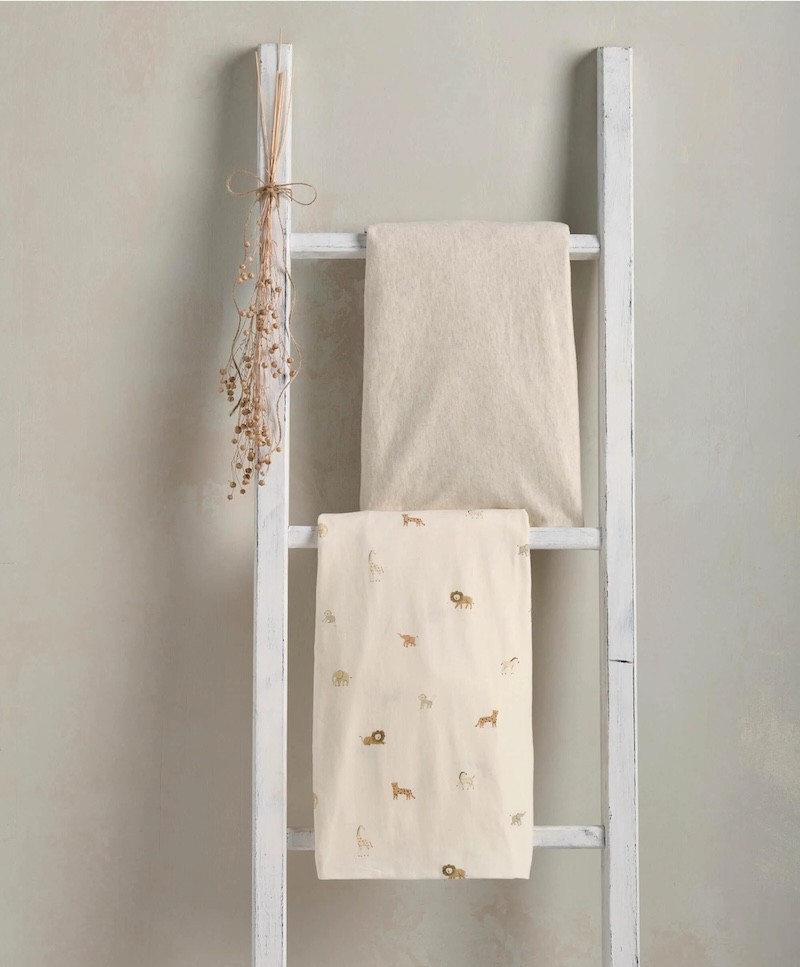 Two baby bedding sheets shown hung over a white ladder