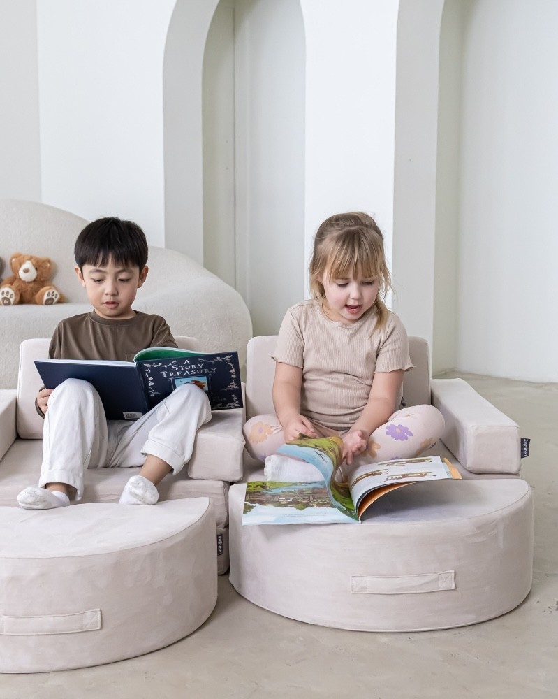 Two toddlers reading books on one of the loungey play couches
