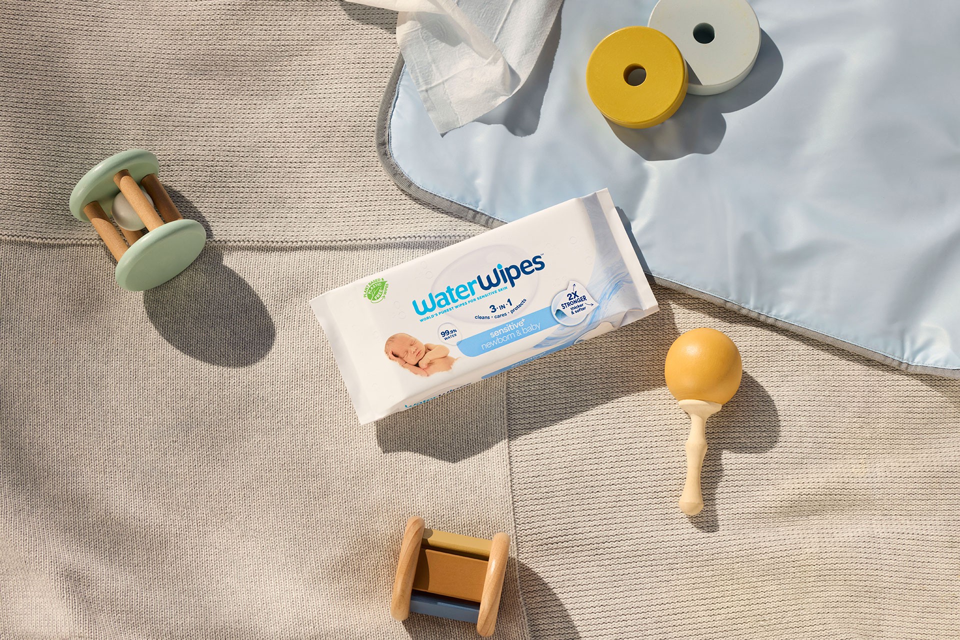 Flat lay of WaterWipes baby wipes and wooden toys on a picnic mat