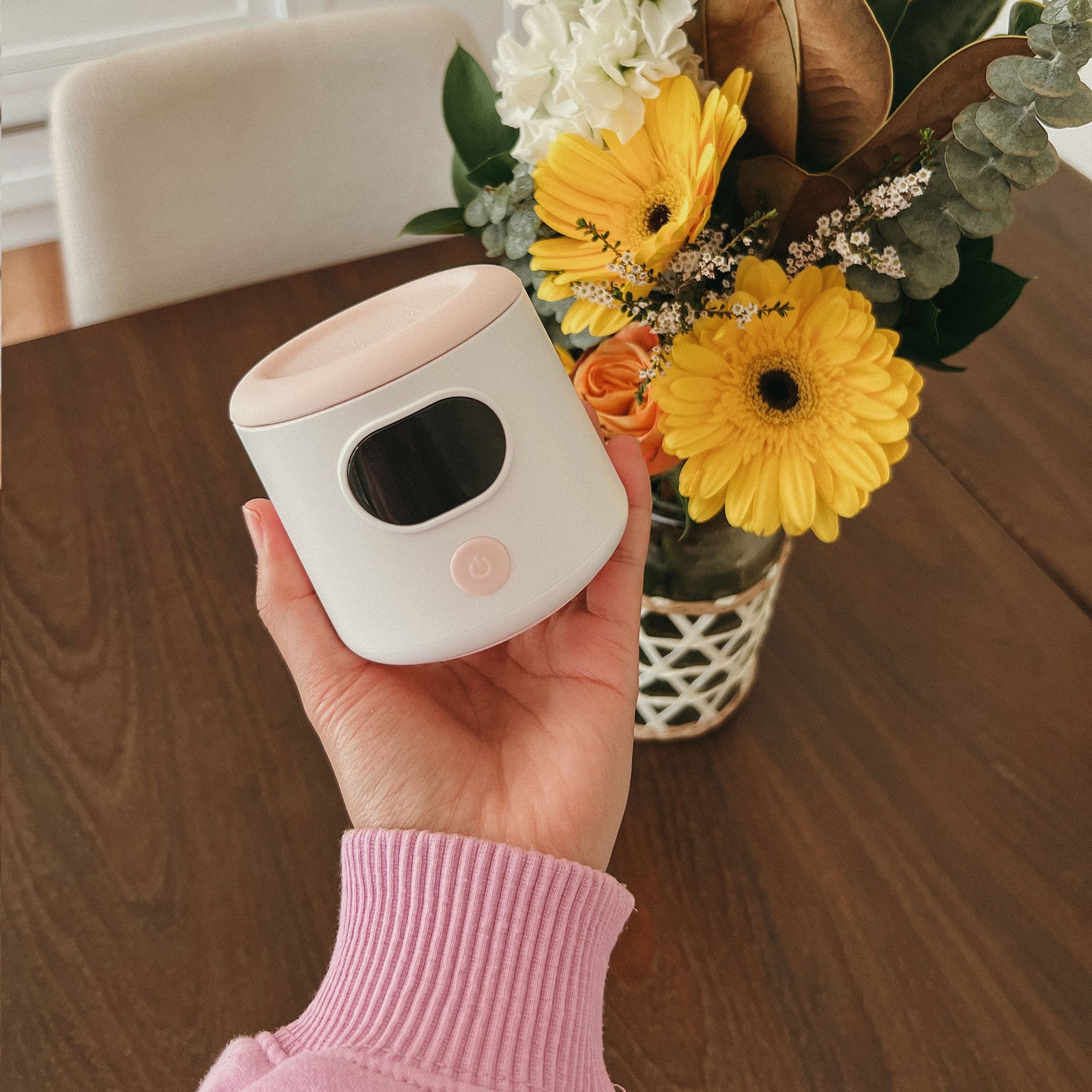 Mum holding a baby bottle warmer with flowers in the background – best bottle warmer for easy, on-the-go milk warming.