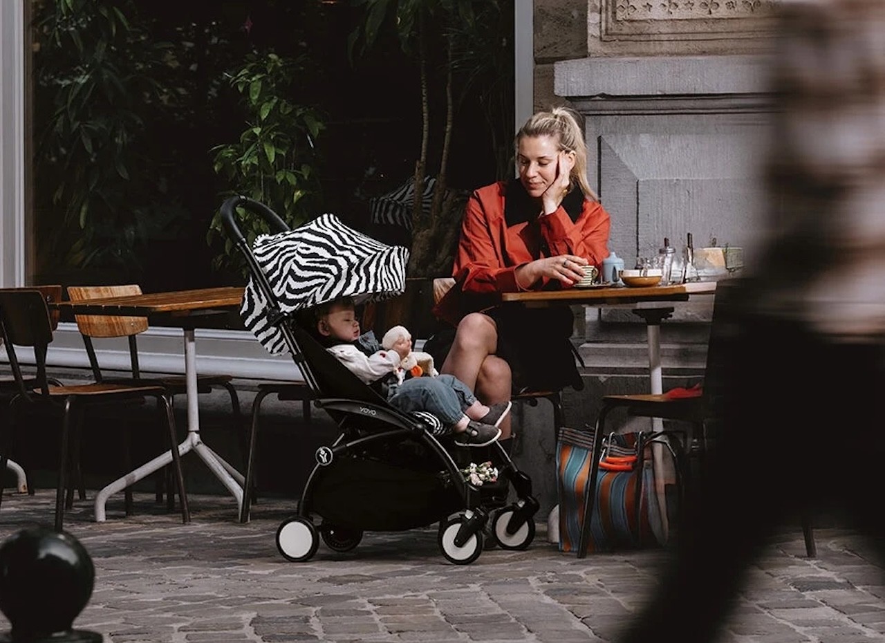 A mum looking at her baby who is sitting in a Stokke Yoyo3 pram with a Zebra print canopy