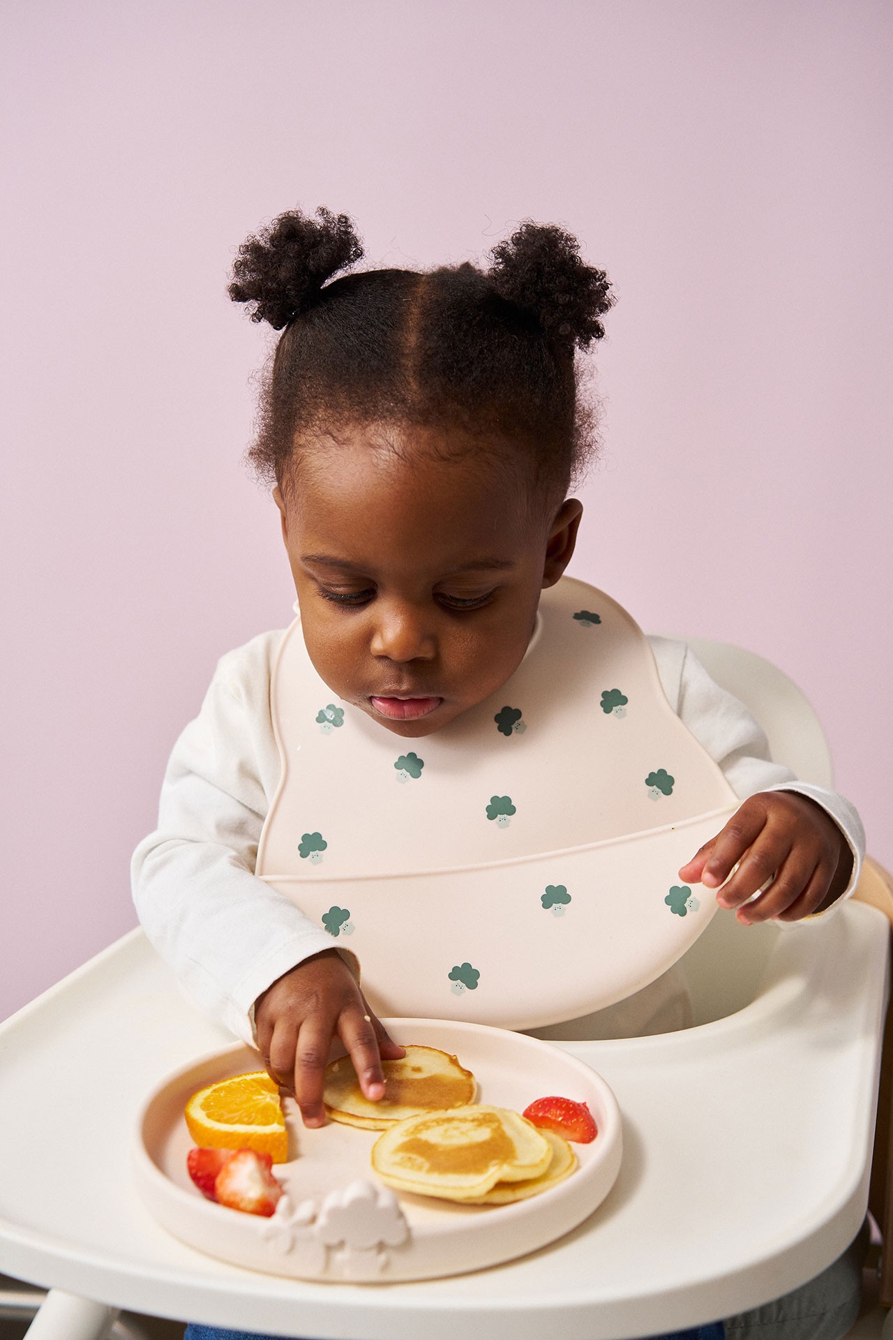 Six month old baby eating strawberry, orange slices and pancakes during the stage when can babies start solids.