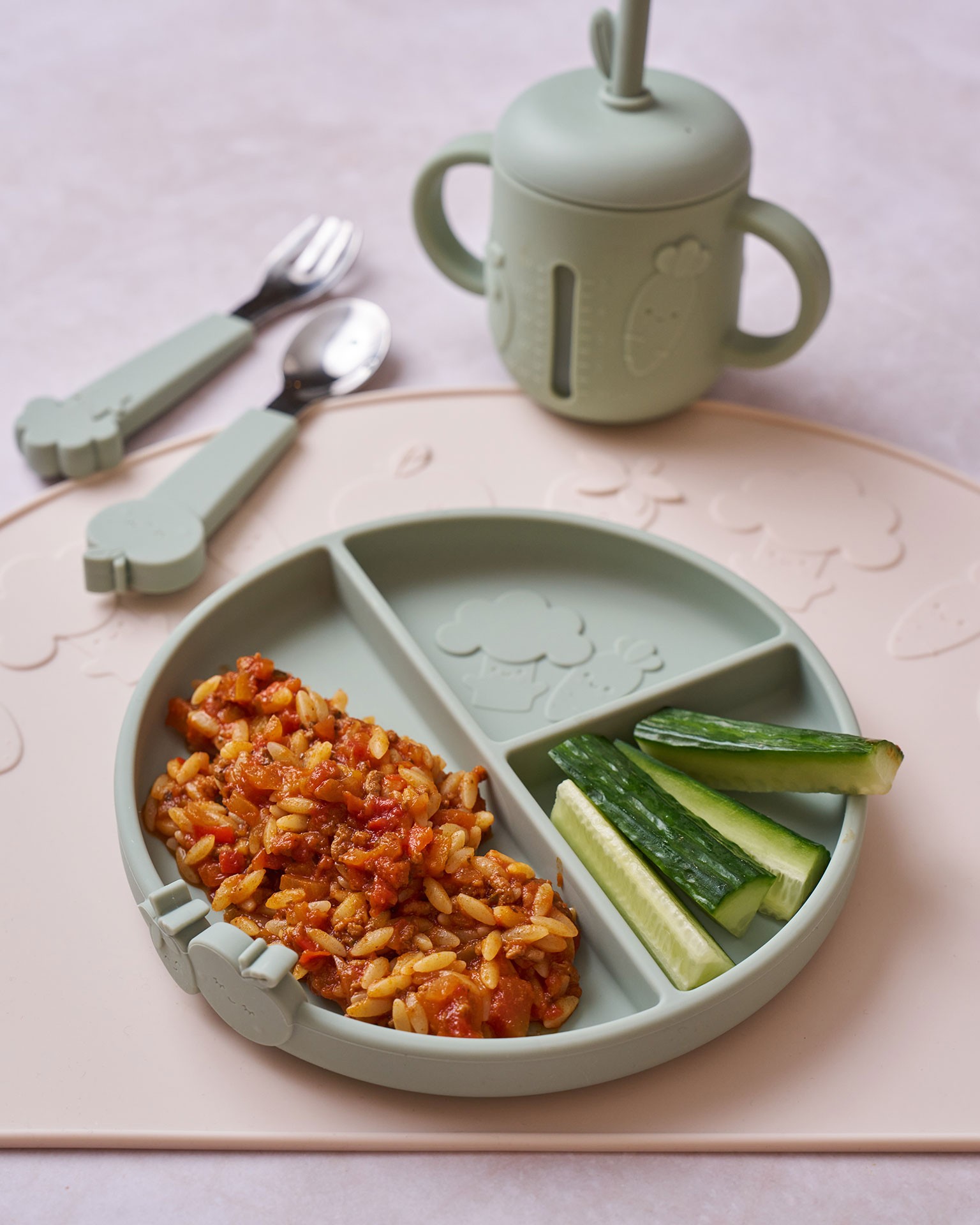 Cucumber sticks and orzo Bolognese served on a green silicone baby plate as baby led weaning foods for starting solids.