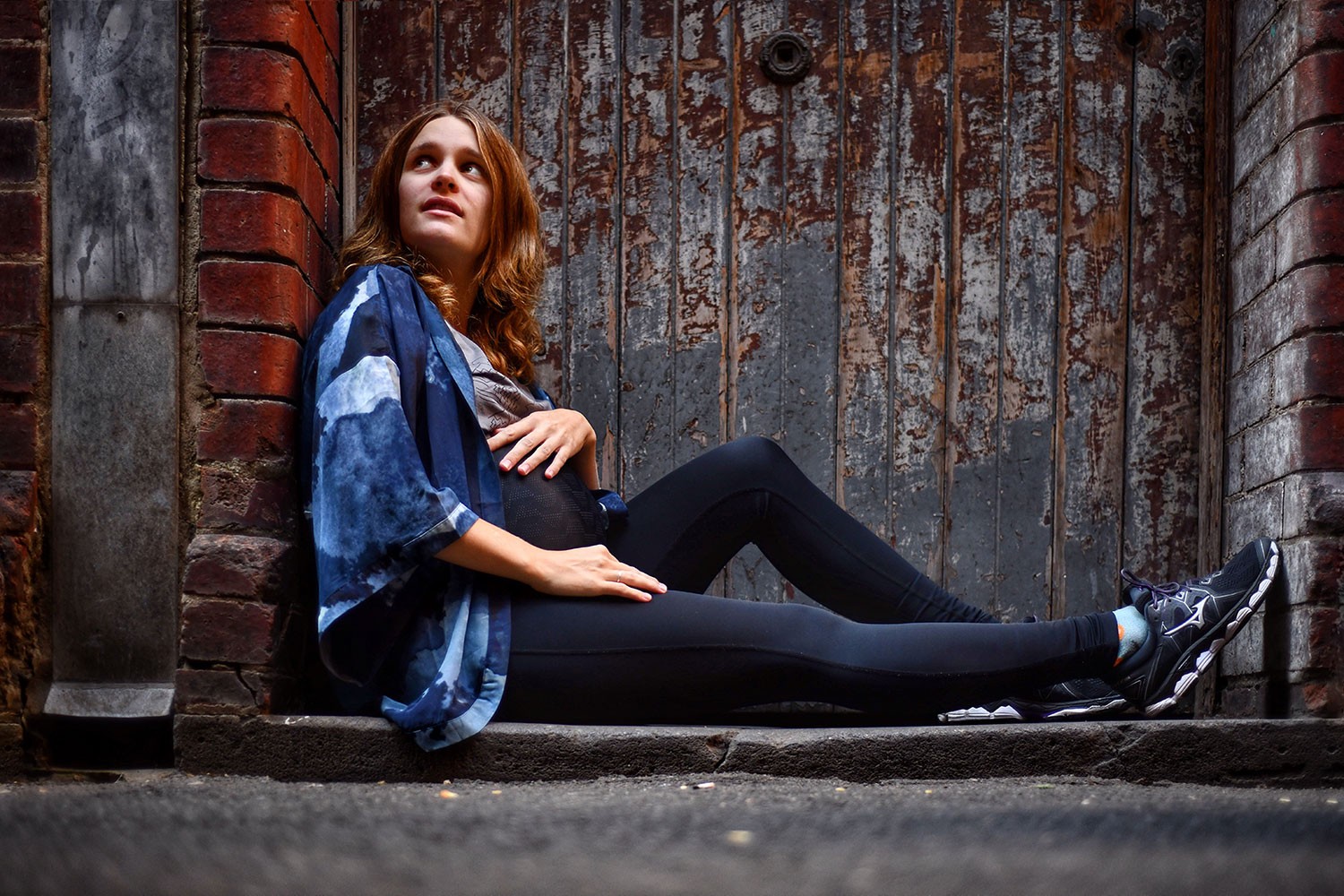 Pregnant woman with a blue shawl seated on a rustic sidewalk, wearing supportive maternity leggings designed to ease bump related issues during pregnancy