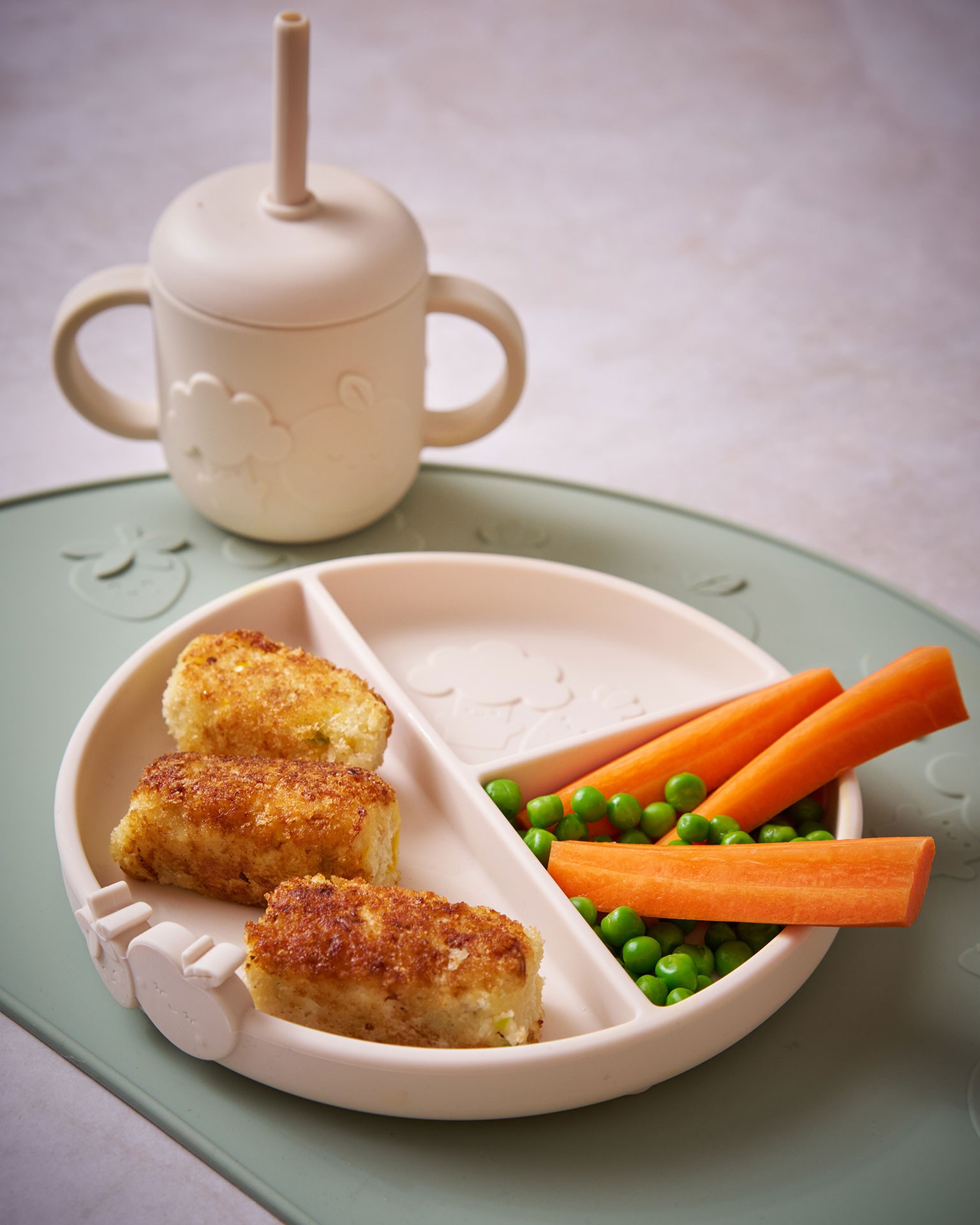 "Finger foods including carrots, peas and chicken arranged on a baby feeding set for baby’s first solid food stage