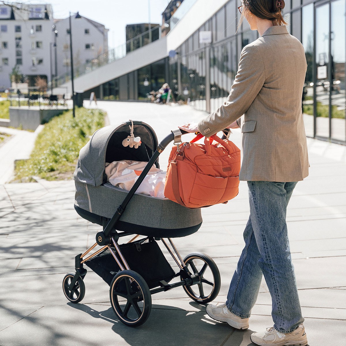 Papaya-hued quilted nappy bag tote secured to pram handle during peaceful walk with sleeping baby in Australia.