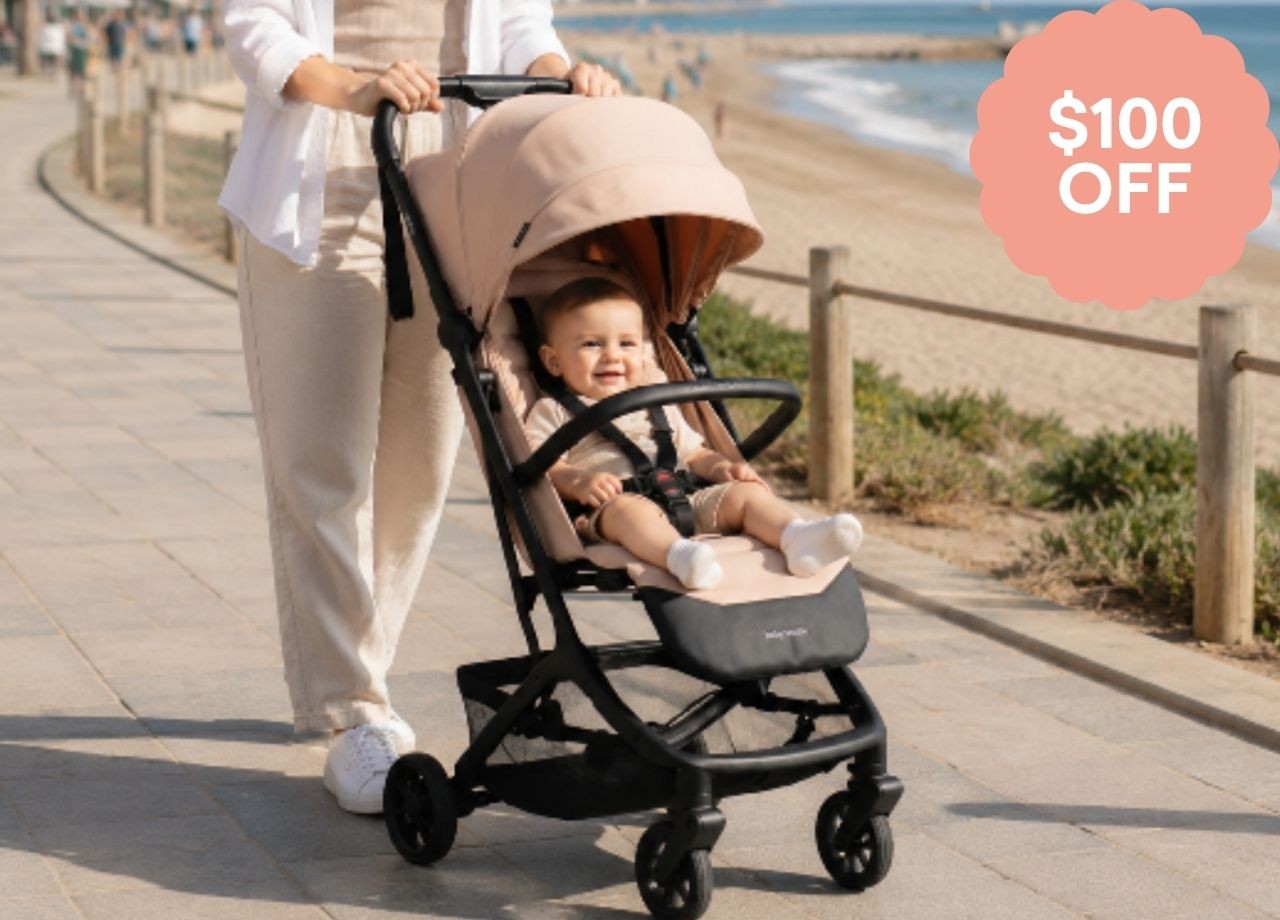 A baby in a travel stroller being pushed by the beach