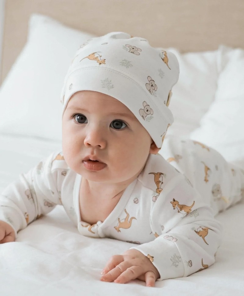 A baby looking at the camera in a zip growsuit and beanie