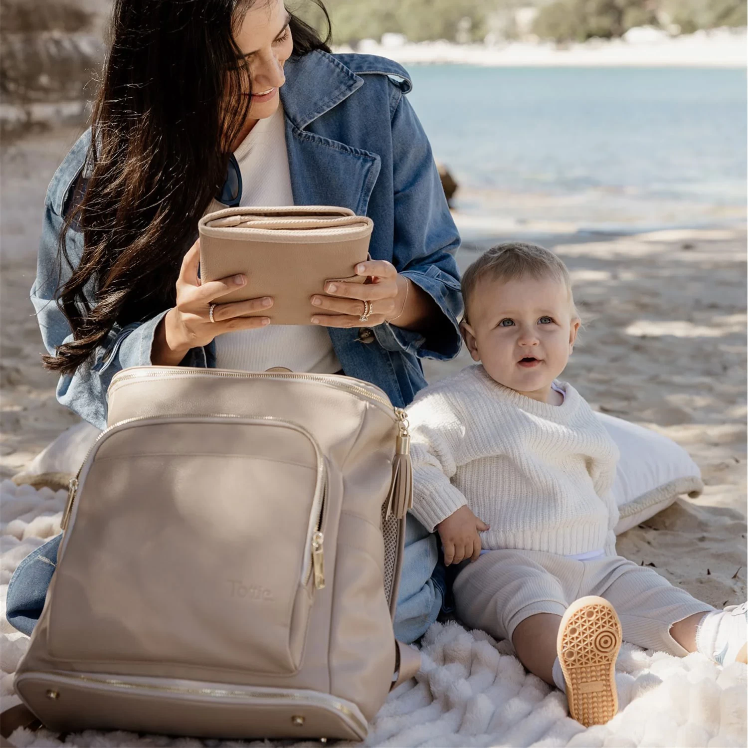 A mum holding a folded Tottie portable change mat with her baby on a picnic blanket