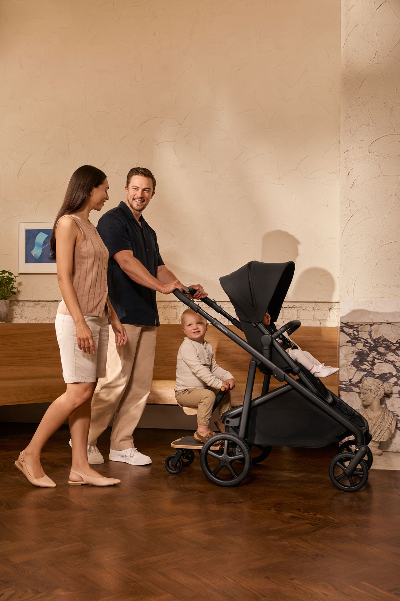 Parents walking and chatting while dad pushes a double stroller carrying their toddler and baby, showing how the best double stroller fits daily life.