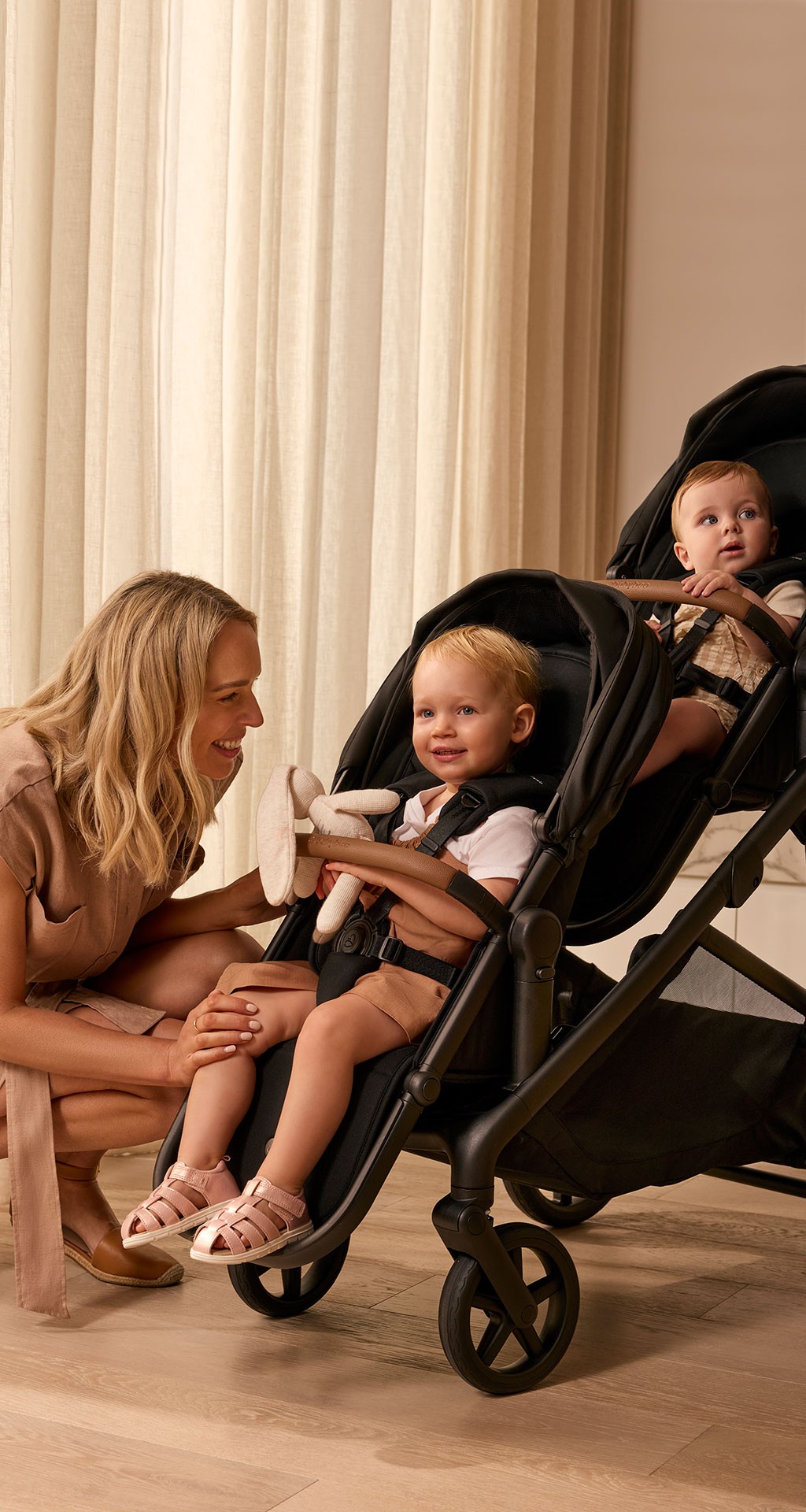 Toddler and baby riding the Babybee Juno double stroller while their mum smiles happily at them.