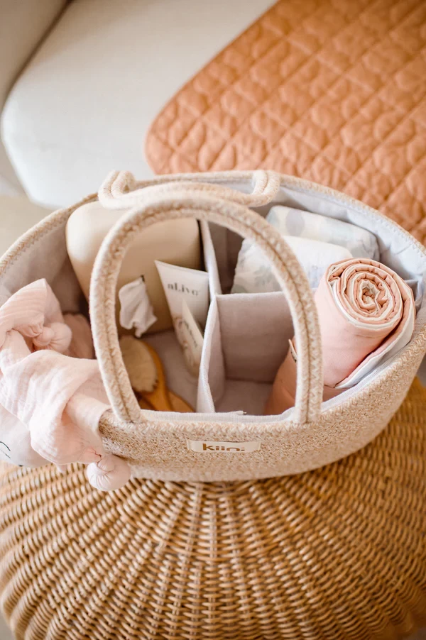 Top view of portable best nappy caddy on rattan chair – filled with swaddle, nappies, baby wipes and essentials for changing on the go