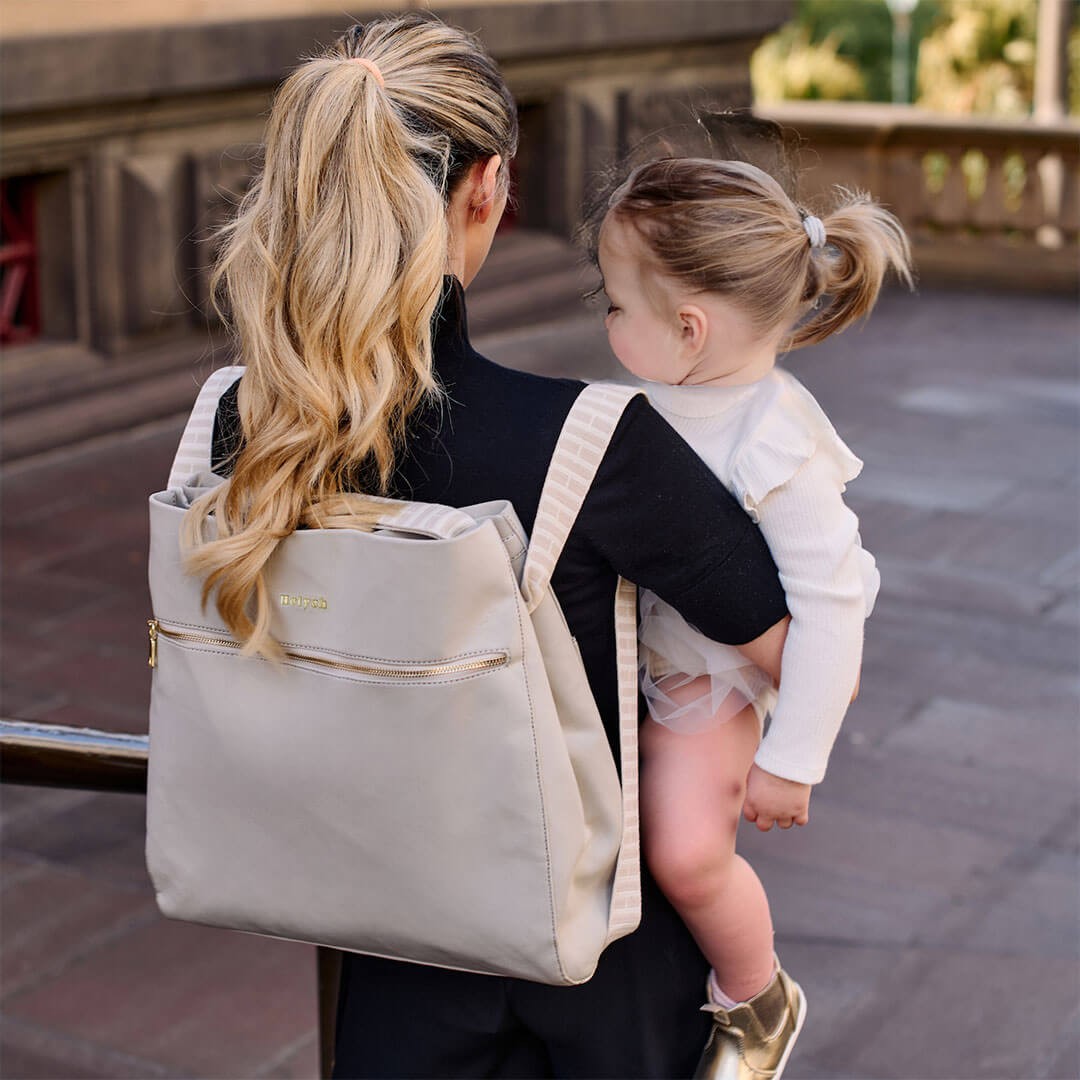 Mum in a black top carrying one of the best nappy bags while holding her baby