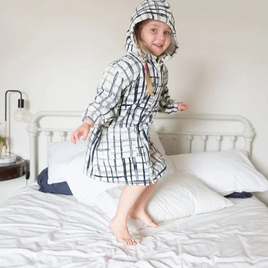 Child on the bed wrapped in a checkered hooded towel, styled as the best hooded  beach towel for kids.