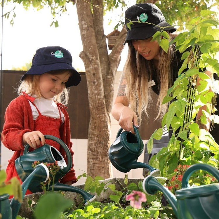 Educator helping a toddler water plants at the best childcare and daycare centre.