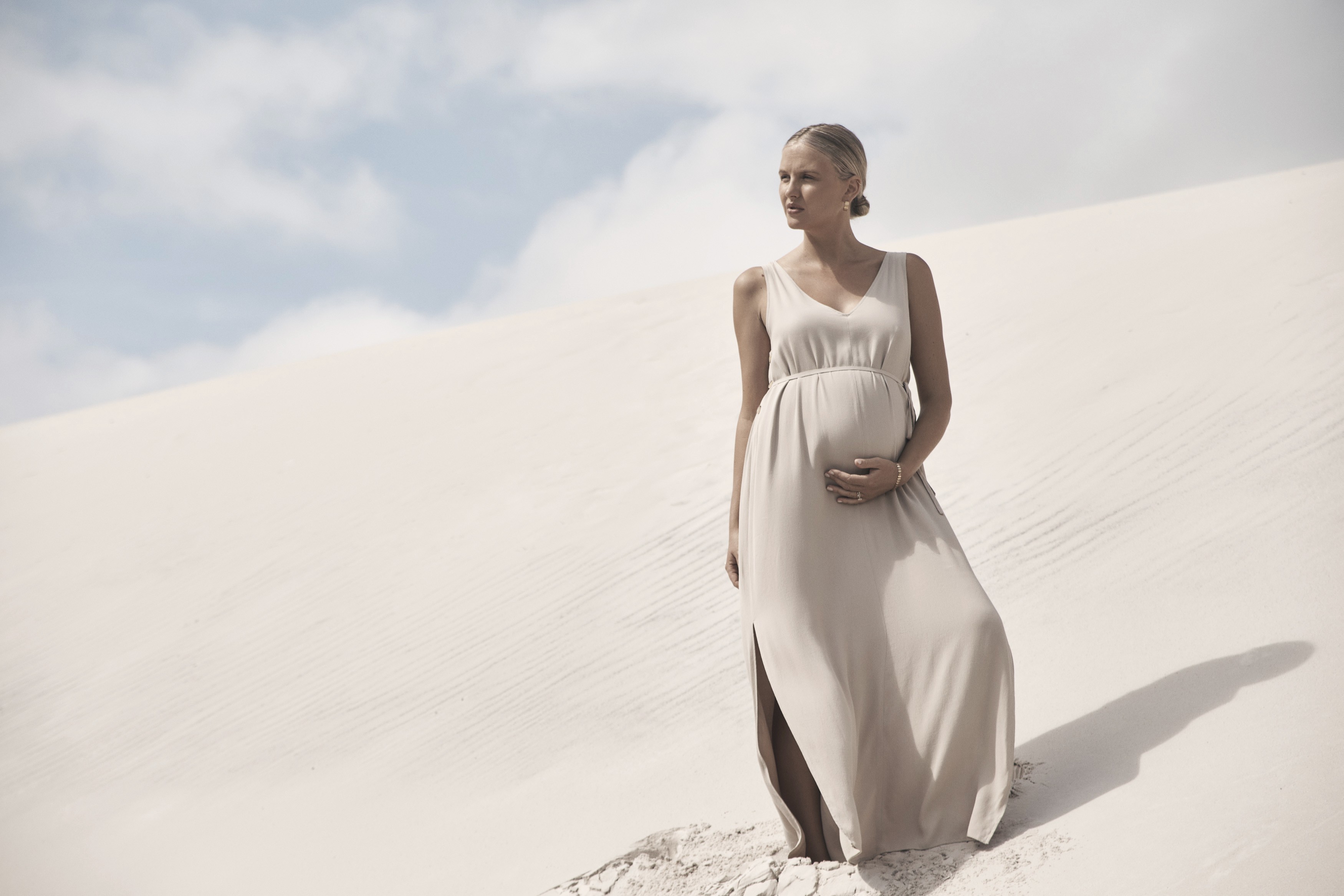 Pregnant mum holding her belly while wearing the LEGOE HERITAGE Camille Maxi Dress in Pumice — stylish and comfortable choice among the best maternity clothes.