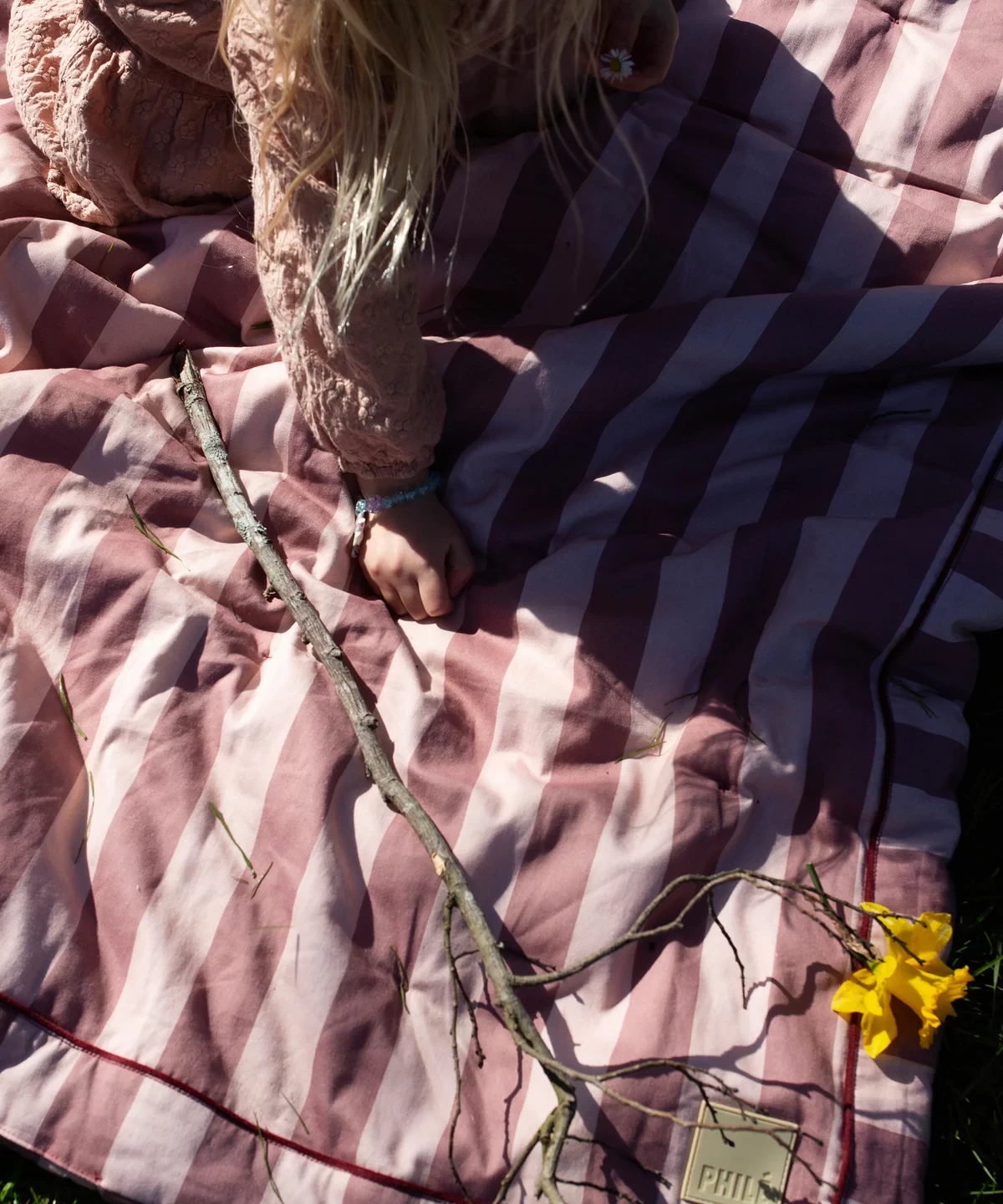 The Phile striped baby play mat outdoors with a child sitting on it playing with wild flowers