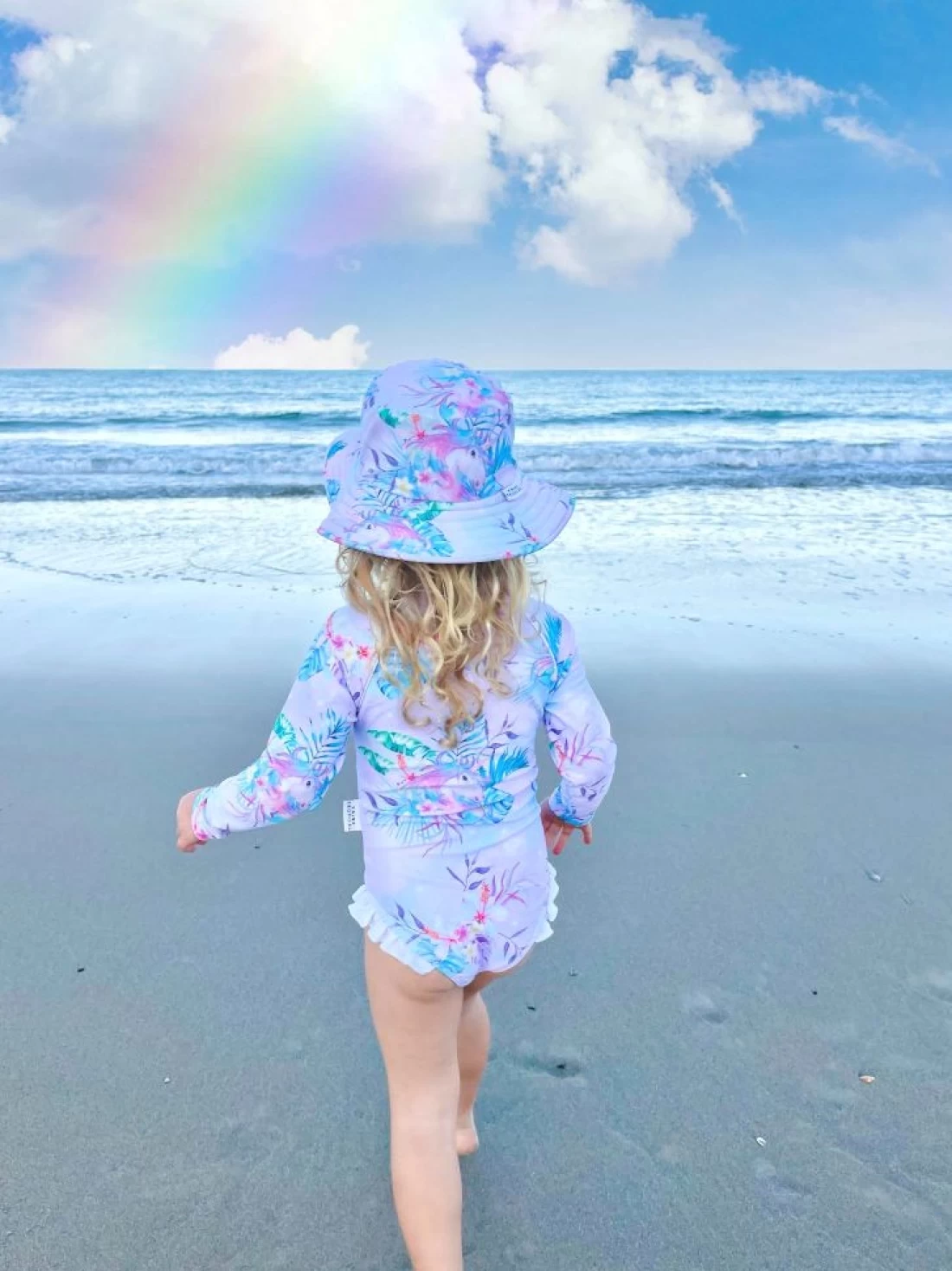 Back view of a girl toddler walking to the beach wearing Tribe Tropical best kids swimwear.