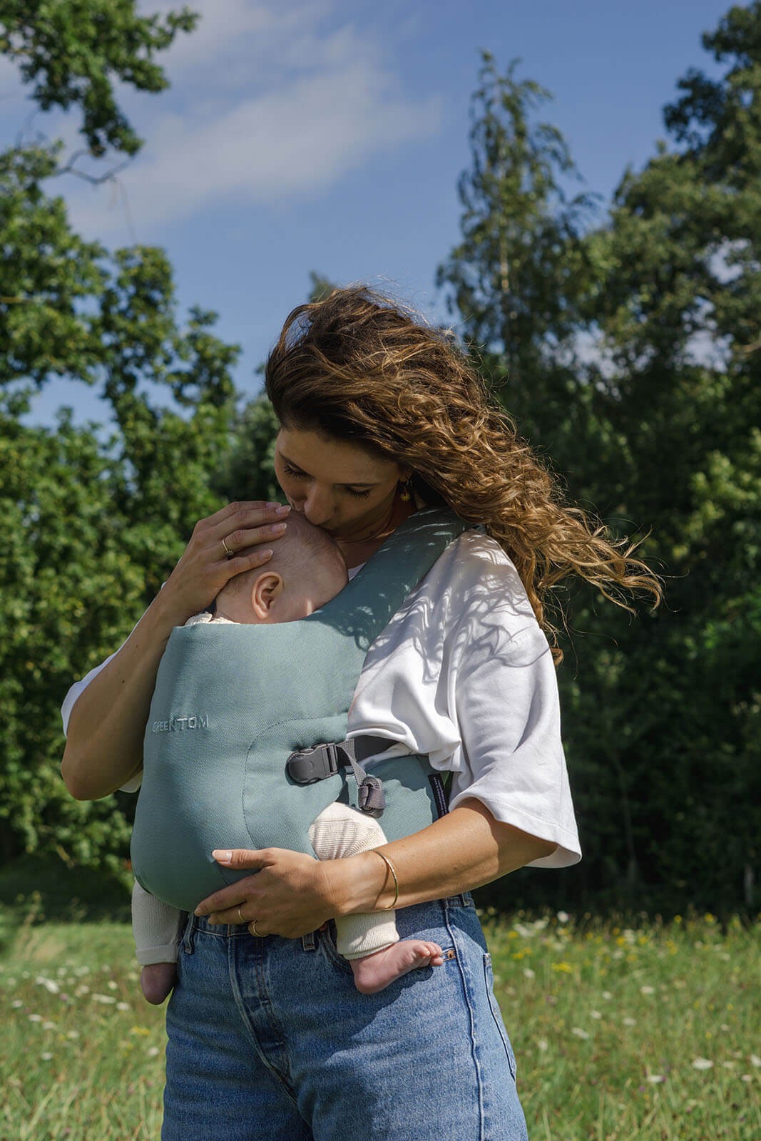 A woman wearing a baby carrier at the park