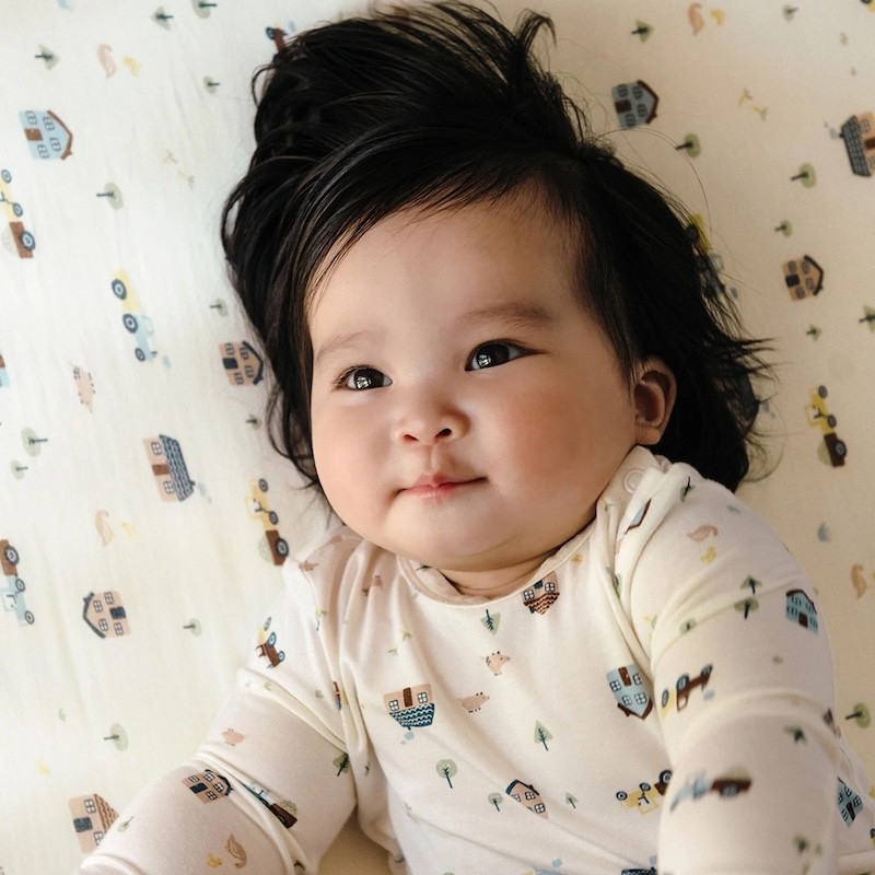 A baby lying on printed cot sheets in a matching onesie