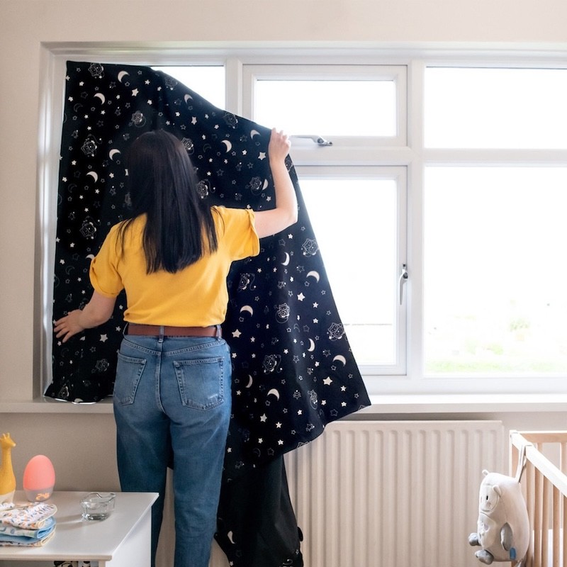A mum hanging up a blackout blind in a baby room