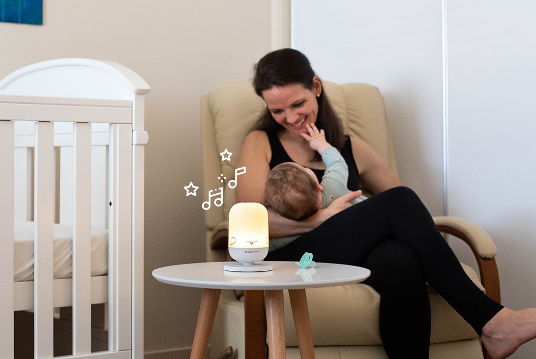 Mum playing with her baby near crib with the best night light glowing on the table.