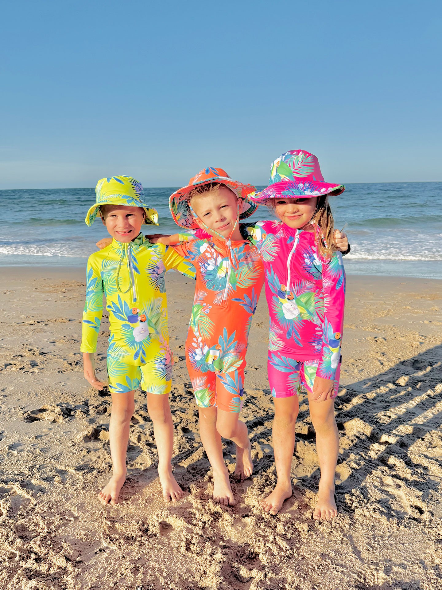 Australian beach scene featuring toddlers in neon kids swimwear in pink, orange, and yellow hues.