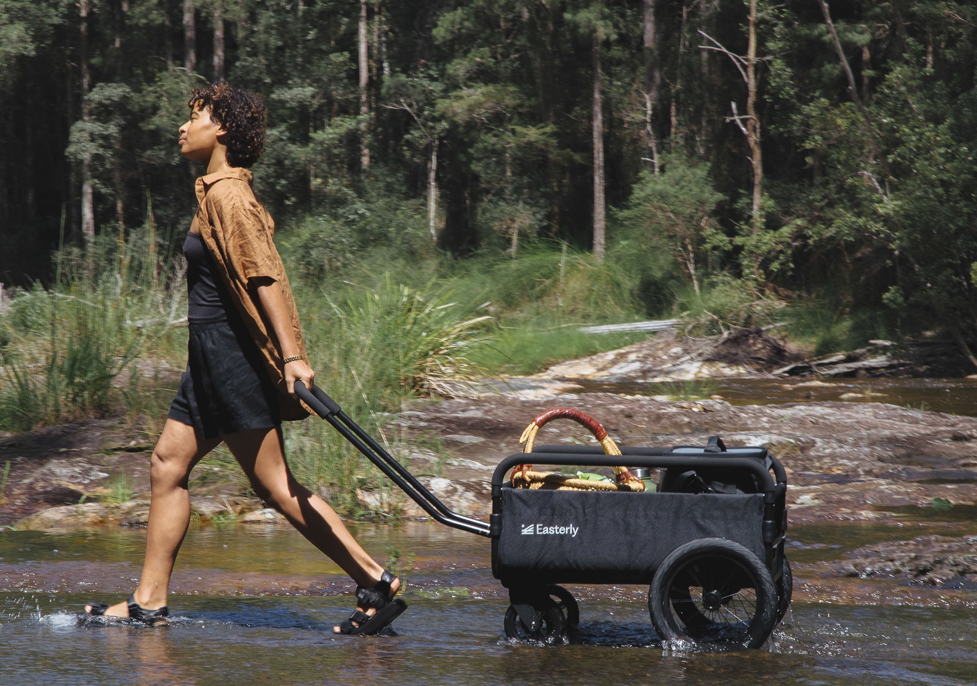 Best beach trolley with strong wheels and high load capacity being pulled across a rocky stream during a camping trip.