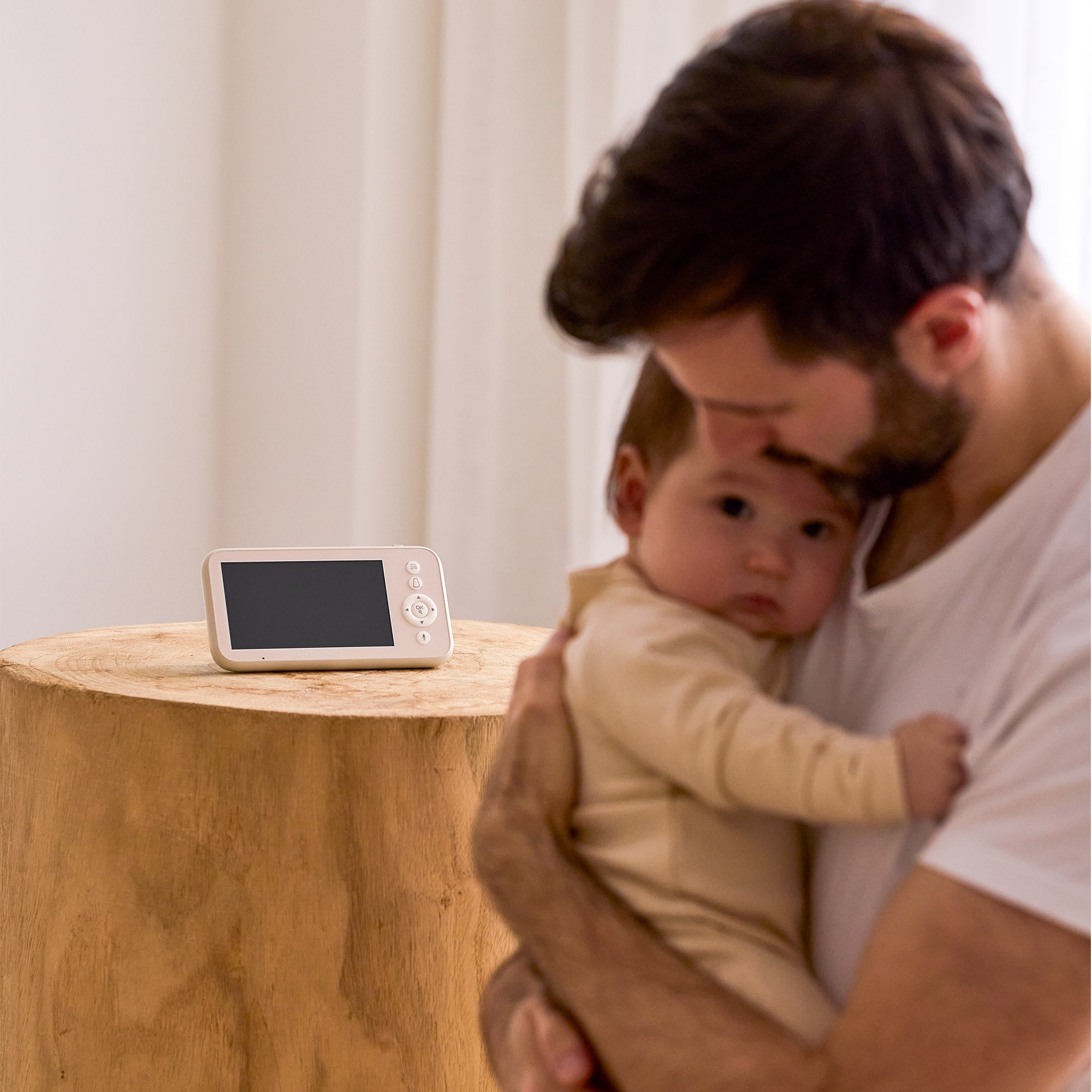 Parent bonding with baby while baby monitor rests on the table behind for safe sleep tracking