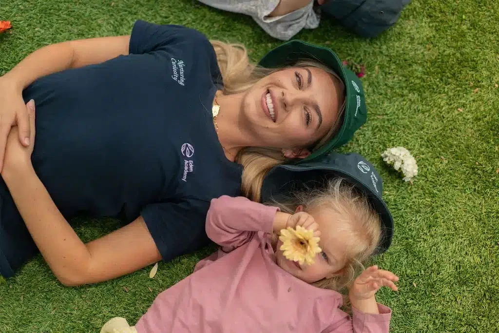Toddler girl lying on the grass with her educator at the best childcare and daycare centre.