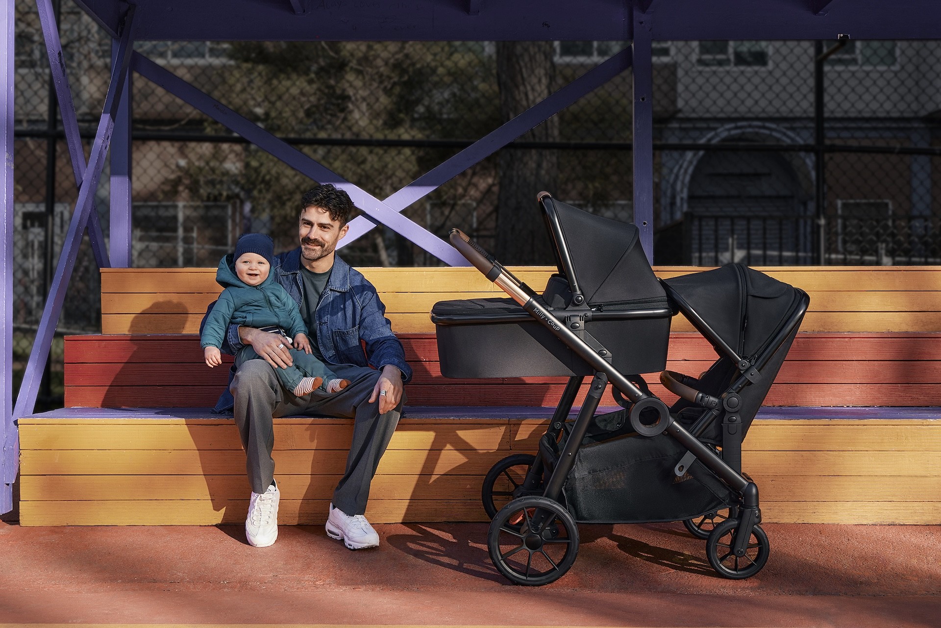 A dad sitting with his baby next to a Milly + Coup pram