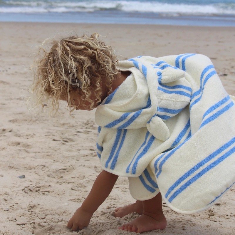 A boy in a sunnylife hooded beach towel at the beach