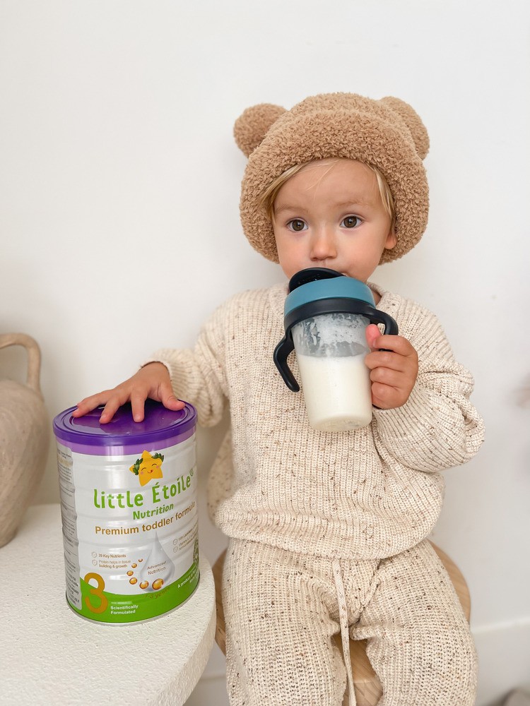 Baby holding can of Little Étoile Nutrition Premium Toddler Formula while feeding from bottle – nutritious toddler feeding moment