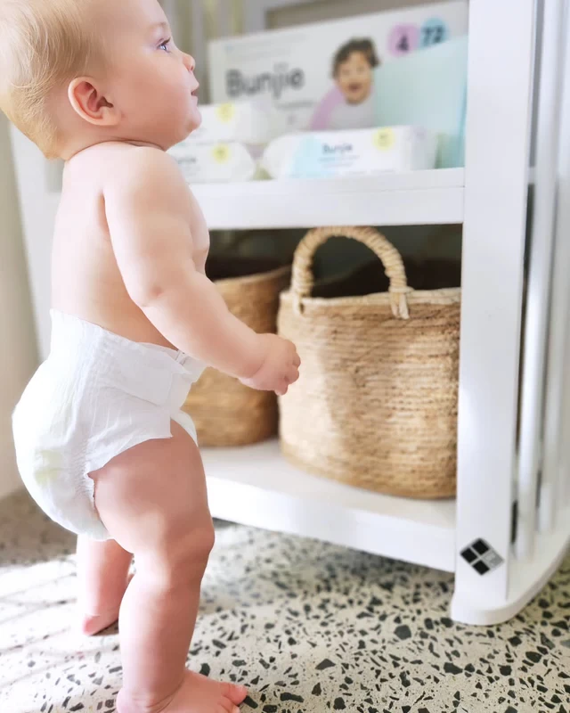 A baby wearing a Bunjie nappy standing next to a nappy caddy