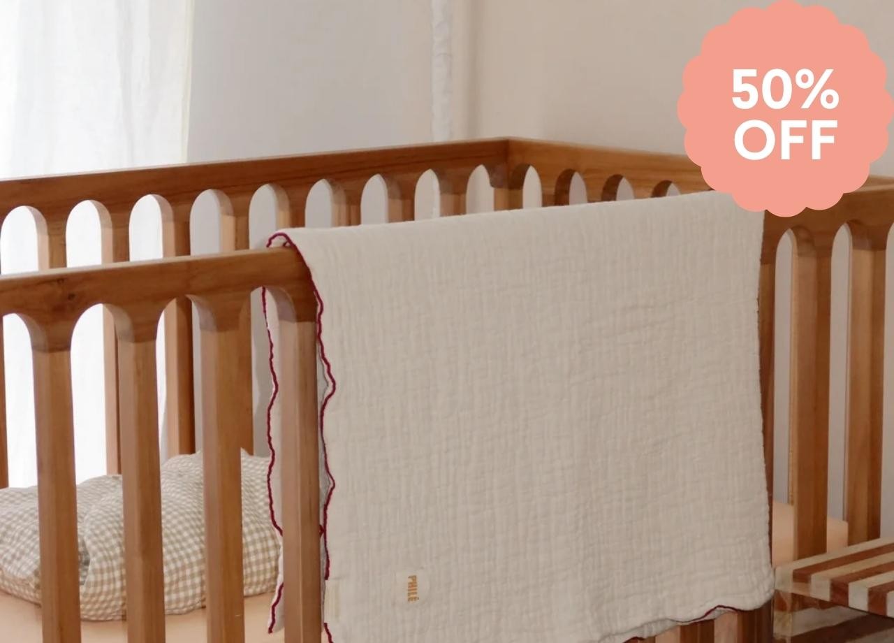 A baby blanket hung over the edge of a wooden crib