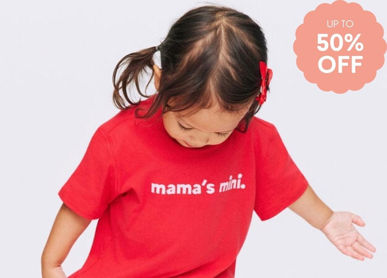 A little girl in a red t shirt that says "mama's mini"