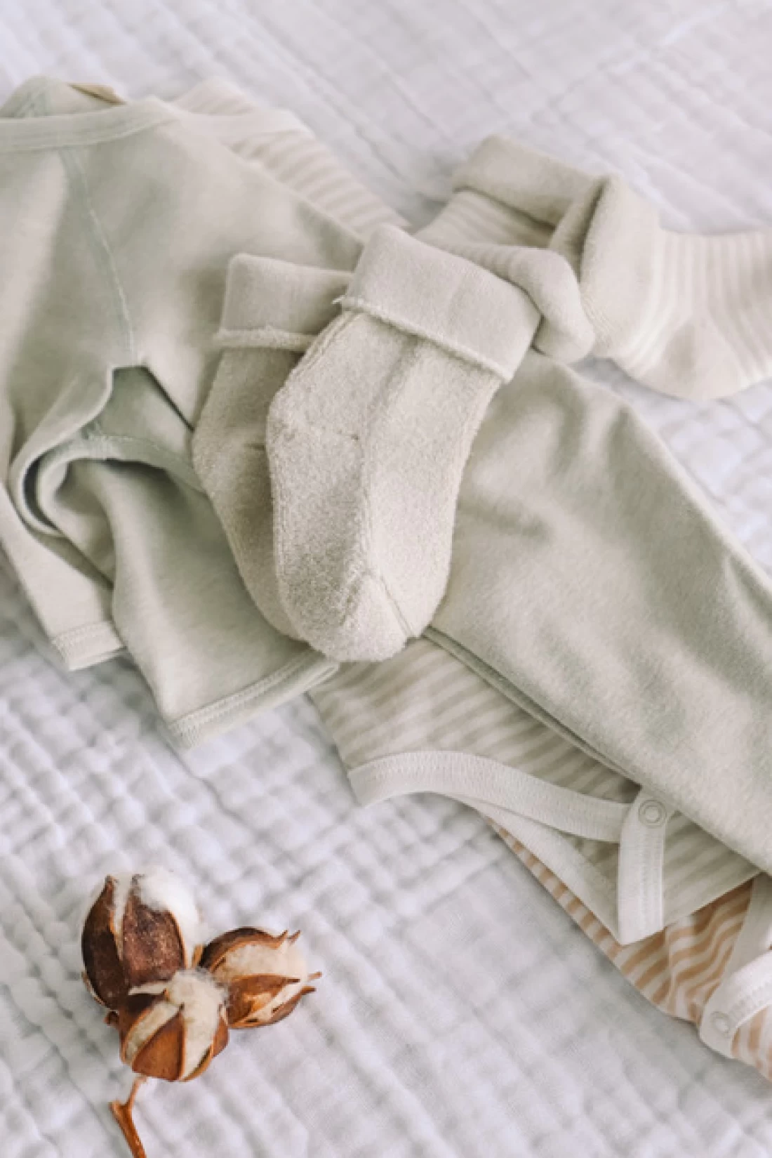 Flat lay of eco friendly baby outfits made from natural fabrics on a bedsheet, highlighting the best eco friendly baby product