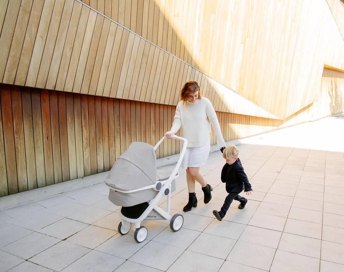 Mum walking hand in hand with her kid while pushing a stroller designed as the best eco friendly baby product