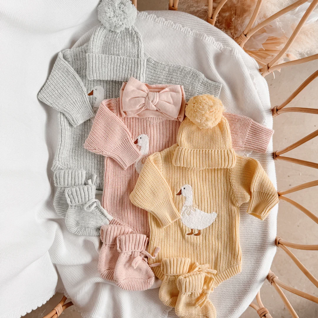 Three baby onesies by blossom and pear laid out on a bassinet