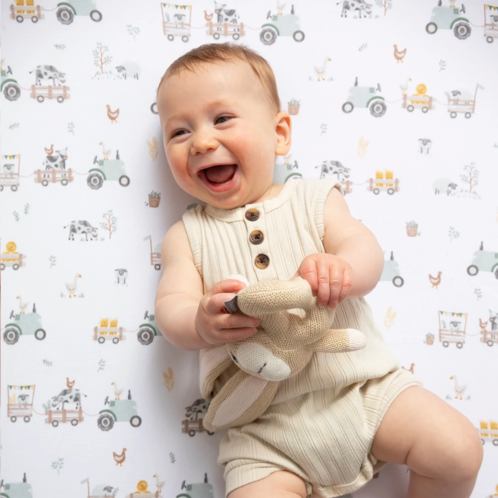 A baby laughing, lying on a cot sheet by living textiles