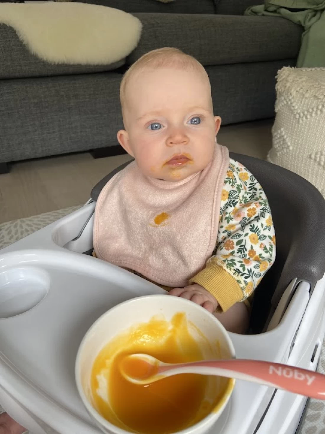 Baby sitting with a plate of food, exploring first tastes as part of introducing solids to baby.