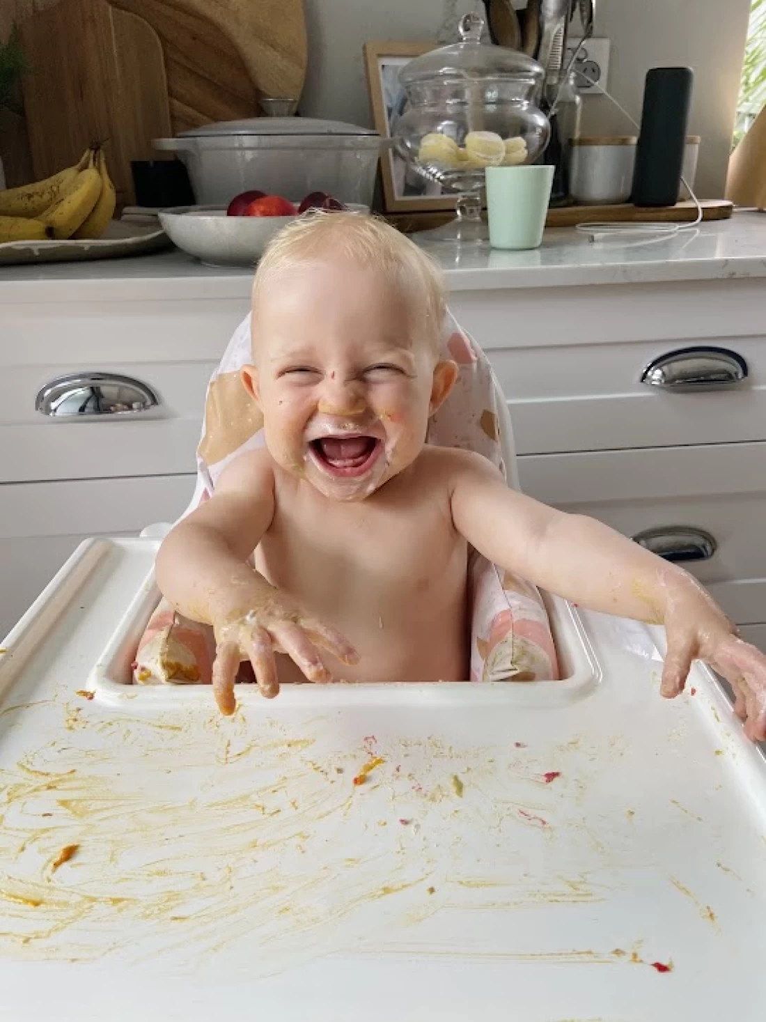 Happy baby sitting at a messy table after eating, showing the fun and challenges of introducing solids to baby.