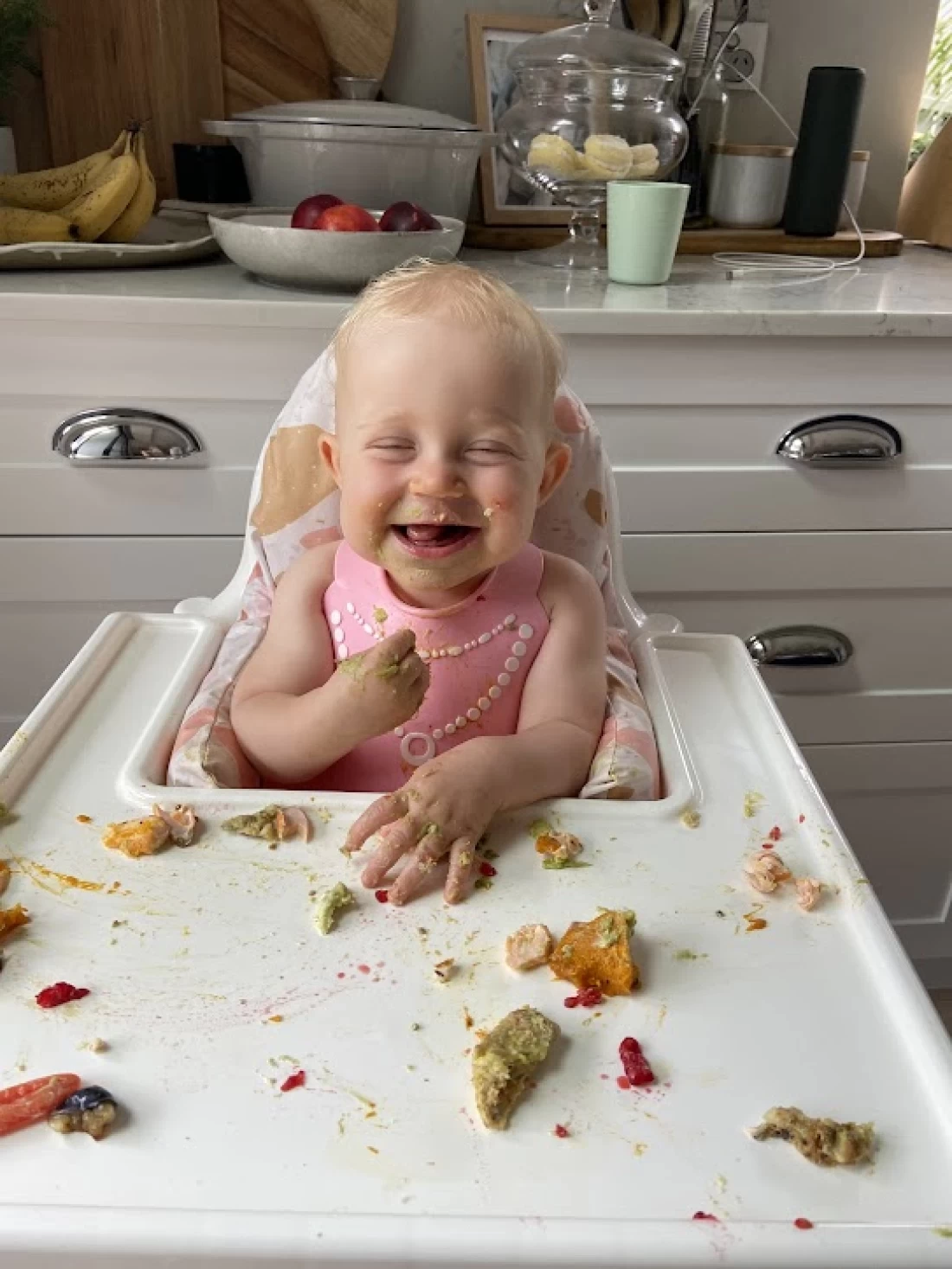 Smiling baby surrounded by food mess, illustrating real-life moments during introducing solids to baby.