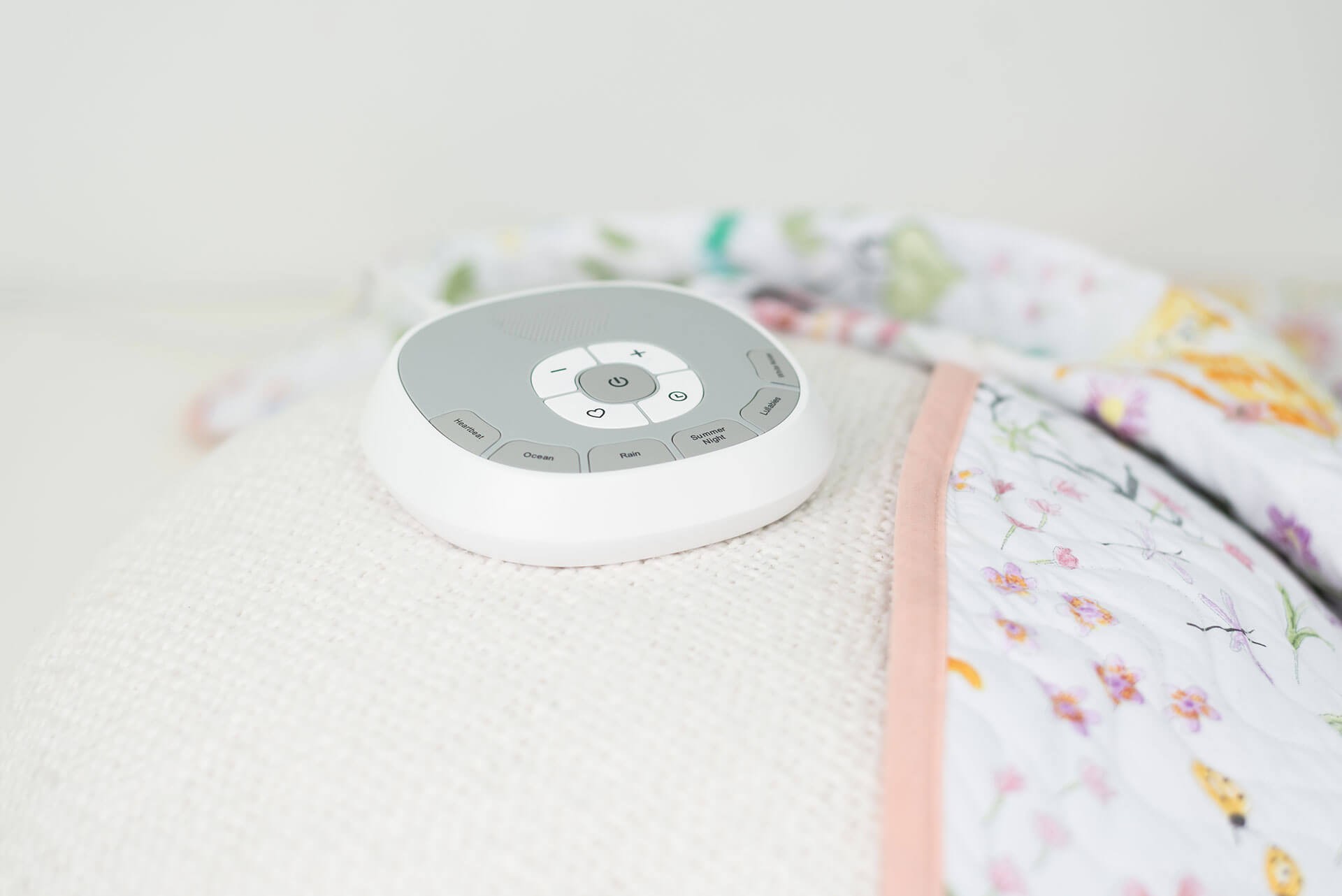 Sound and sleep machine in neutral grey shade placed on cosy knotted throw – essential for newborn sleep support.
