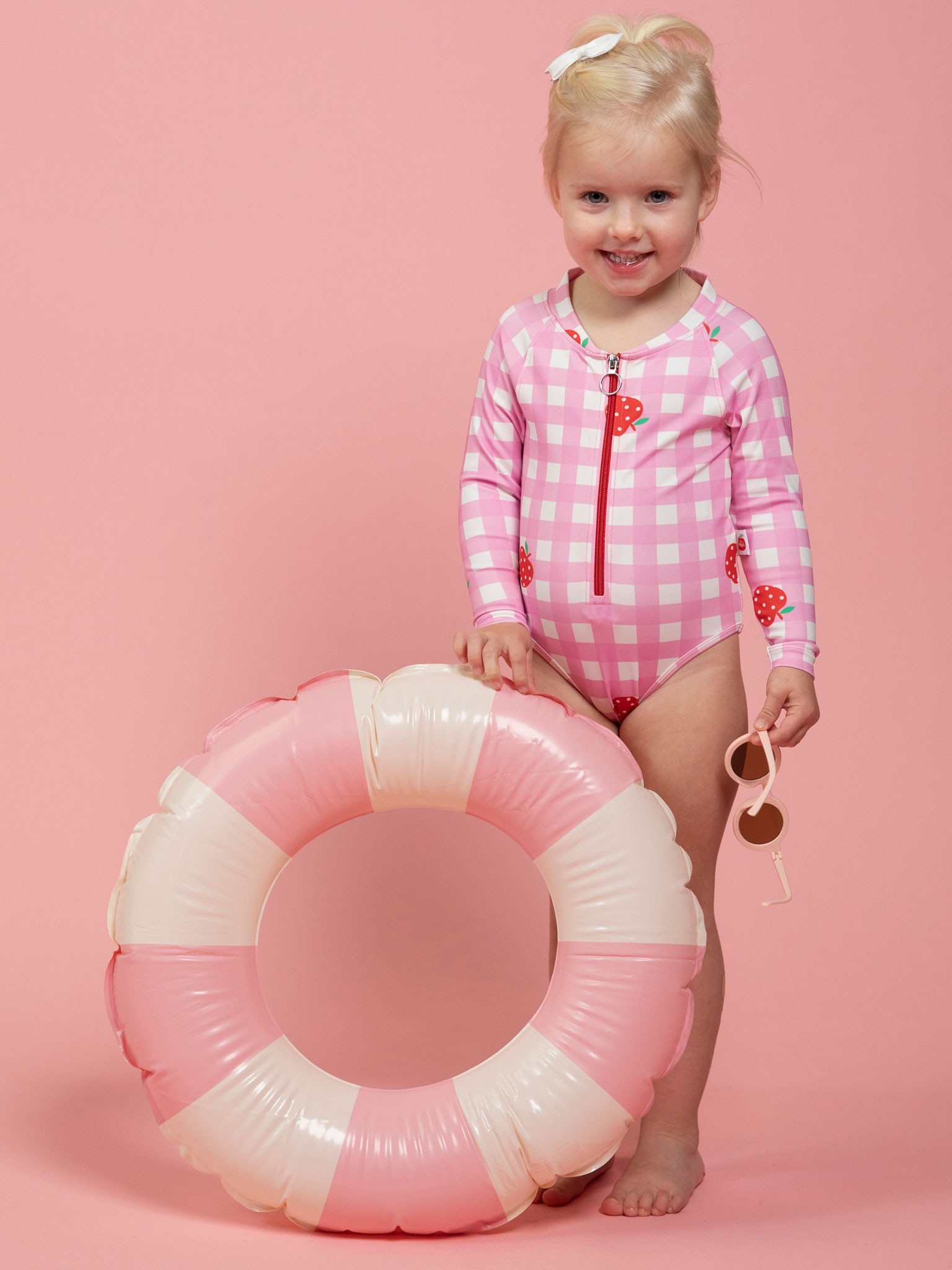 Toddler in Oobi’s pink gingham swimsuit holding a pool floatie – playful look from one of the best baby clothes brands.
