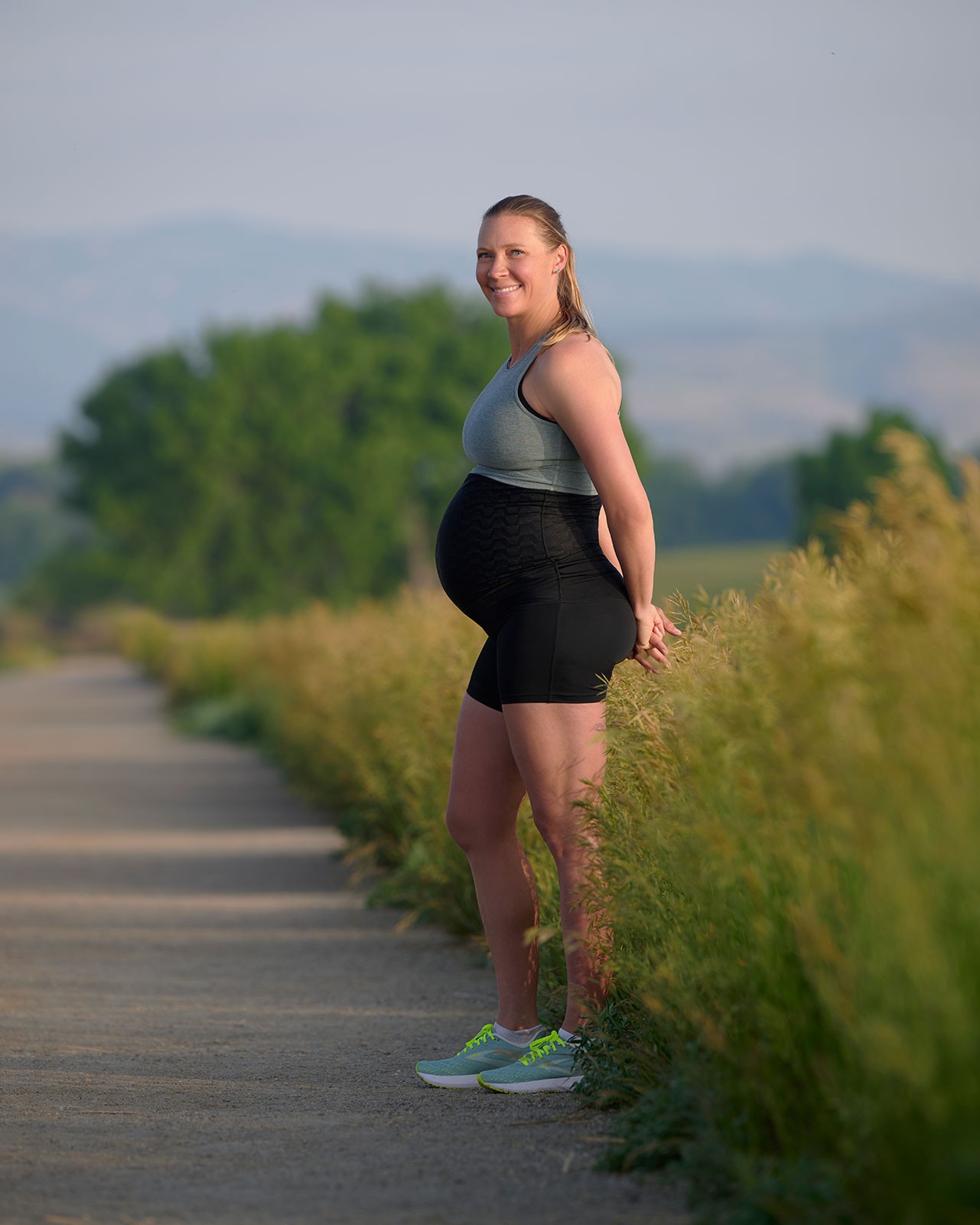 A pregnant lady wearing a grey tank top and black pregnancy shorts on a driveway, highlighting comfort and support for bump related issues during pregnancy.