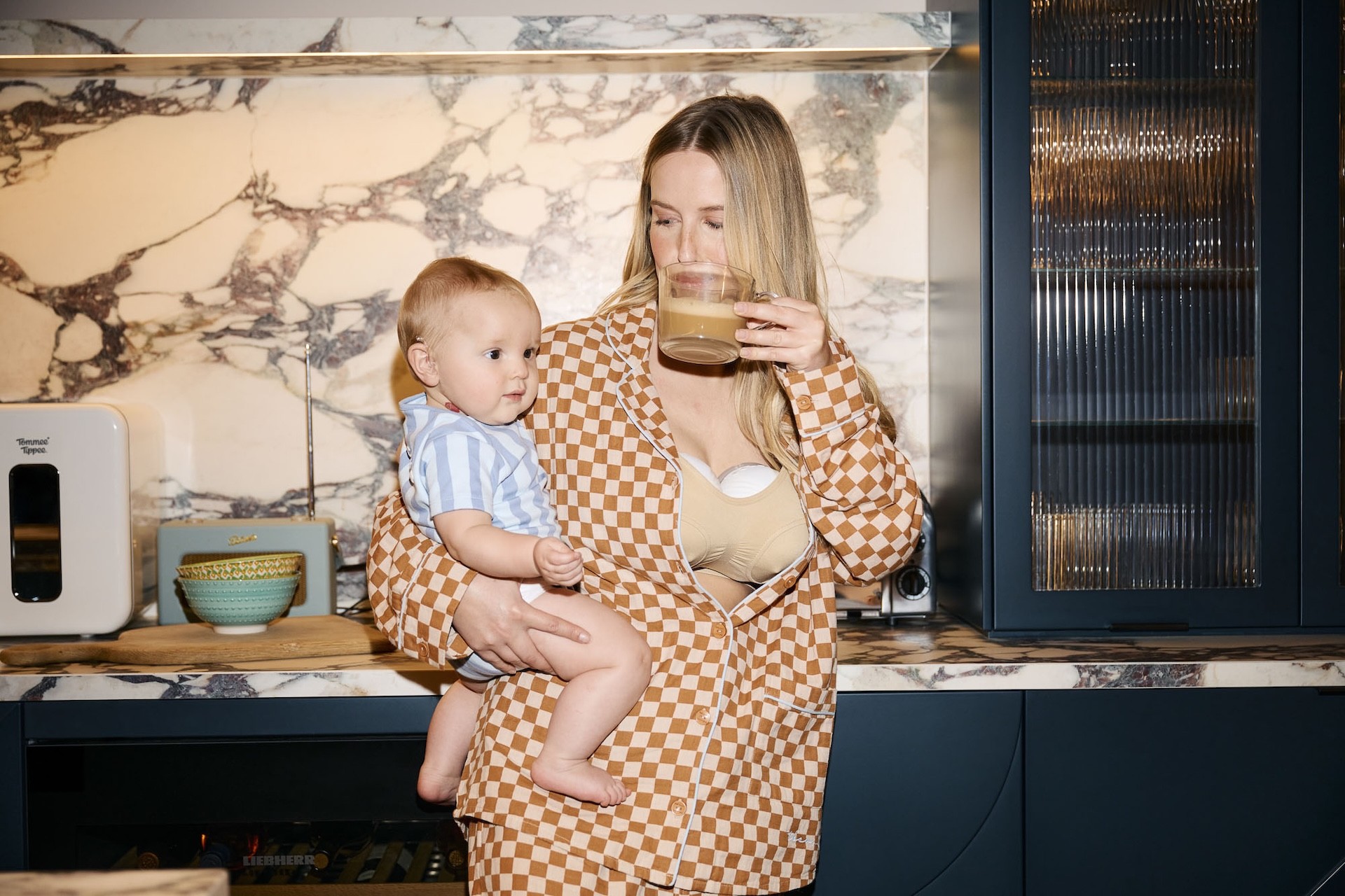 An Australian Mum wearing the Tommee Tippee Double Wearable Breast Pump while sipping a coffee and holding her baby