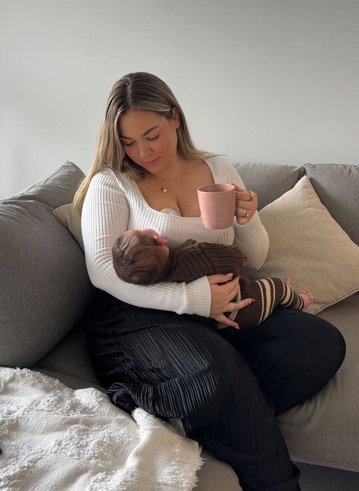 Mum holding newborn baby boy while using best wearable breast pump in Australia, enjoying a quiet coffee on the couch.